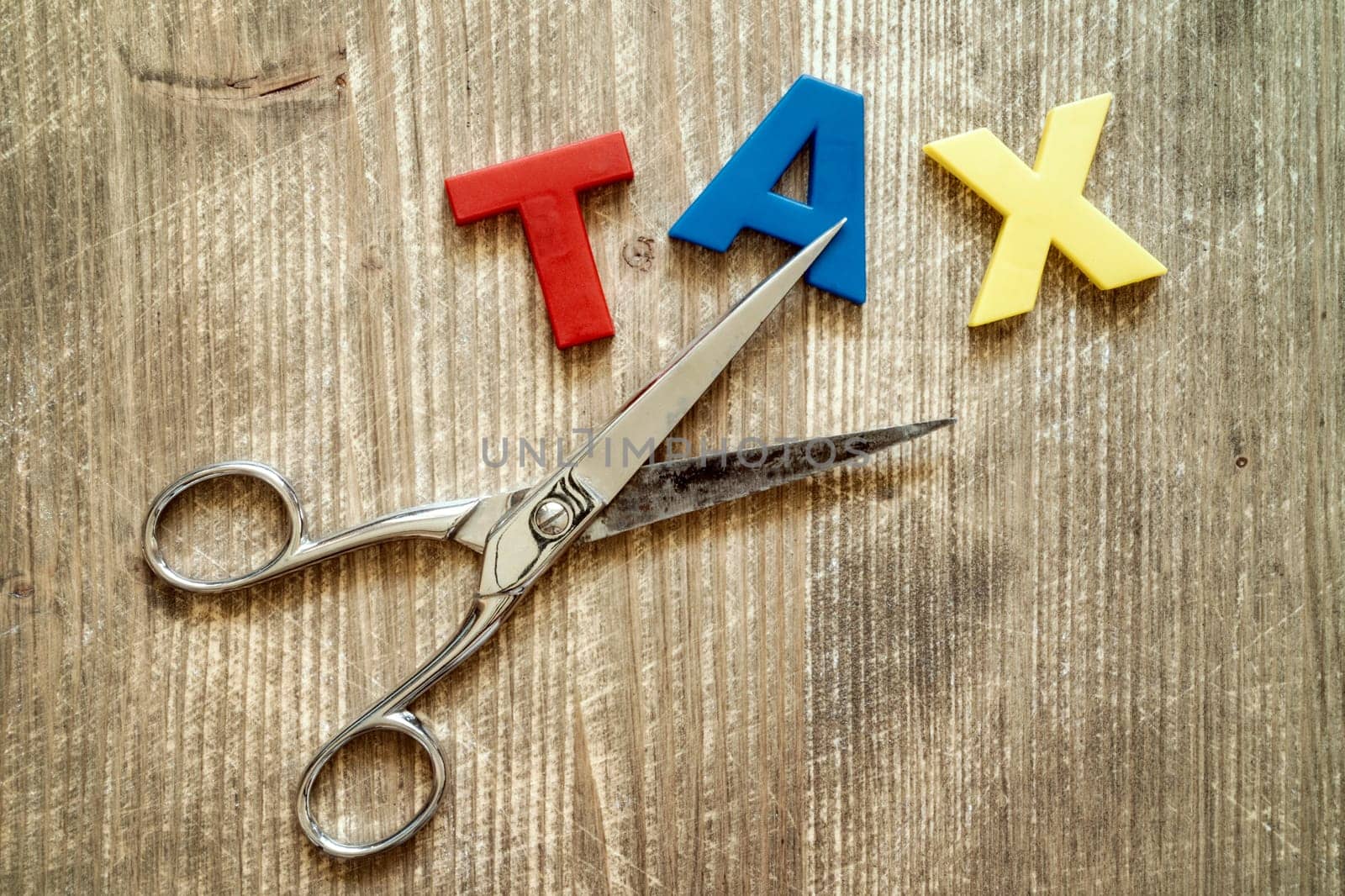 Cut of tax Concept. Scissors and the colorful plastic alphabet on wooden background.