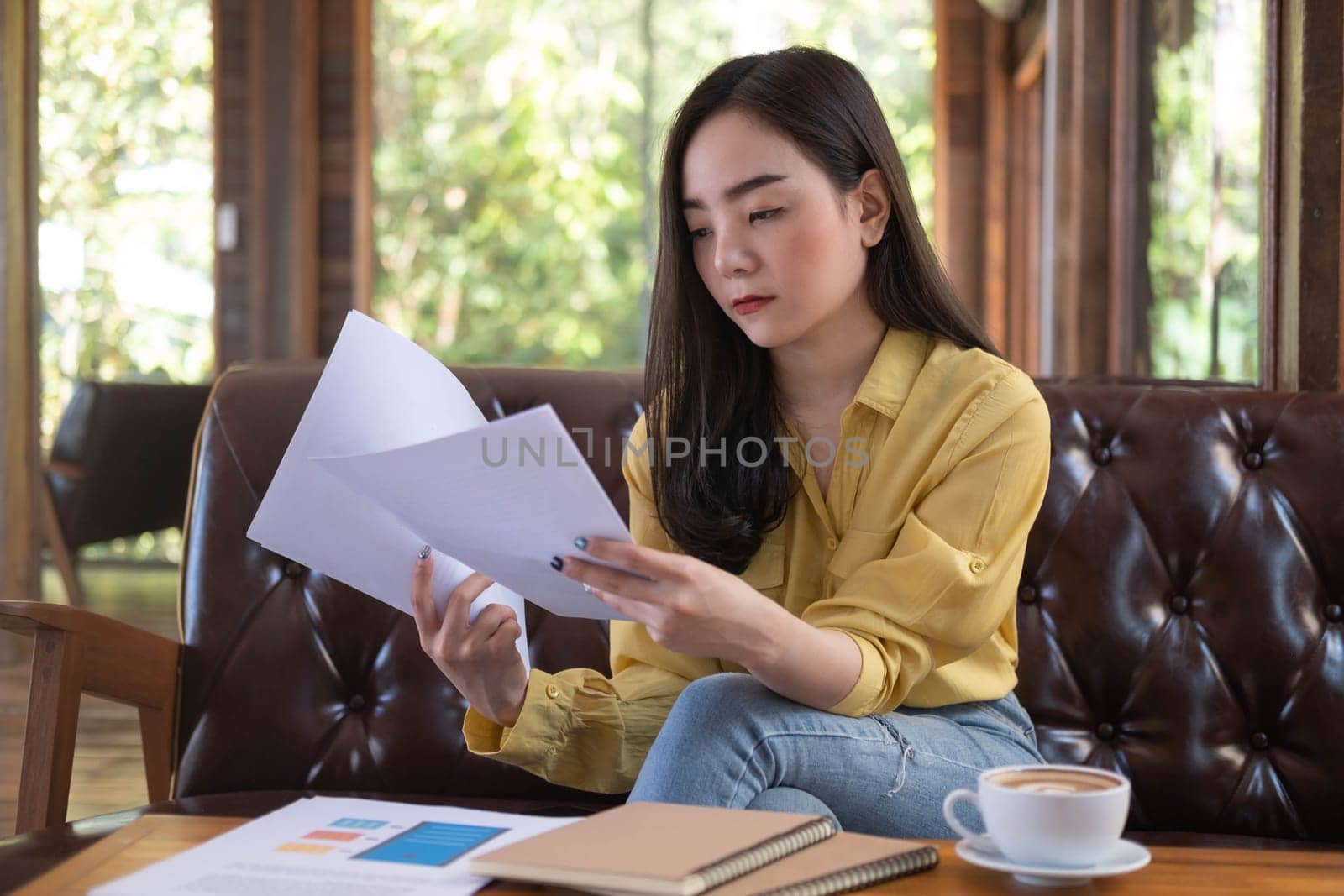 Young Asian businesswoman sitting in cafe and reading documents. Female working with financial documentation and financial reports before meeting.