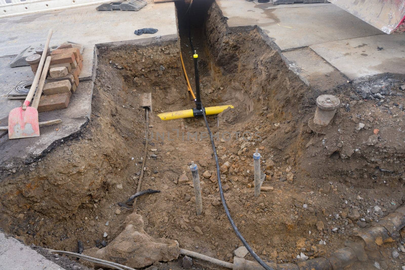Work on the installation of engineering and heating systems. Two plastic pipes one yellow for gas pipe and one black for power lines. They are in a sand ditch.