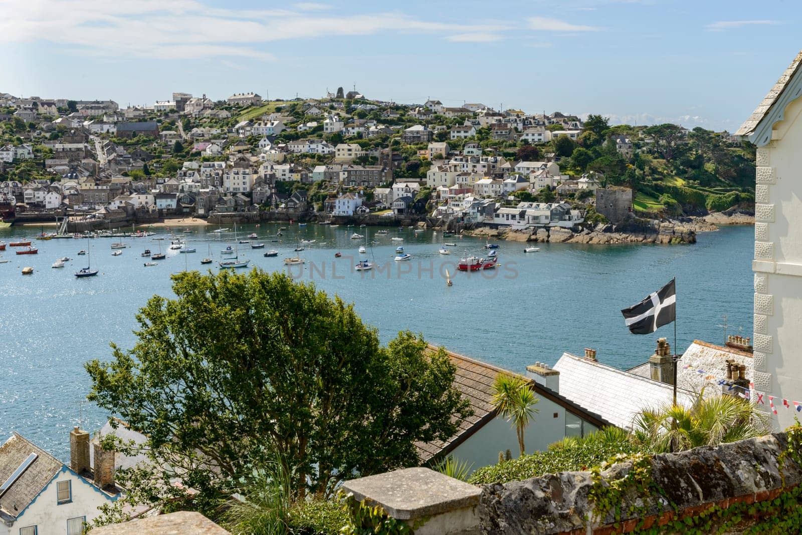 view of cove harbour and village on southern coast of Cornwall, shot from the opposite side of the cove whit a flag in foreground.