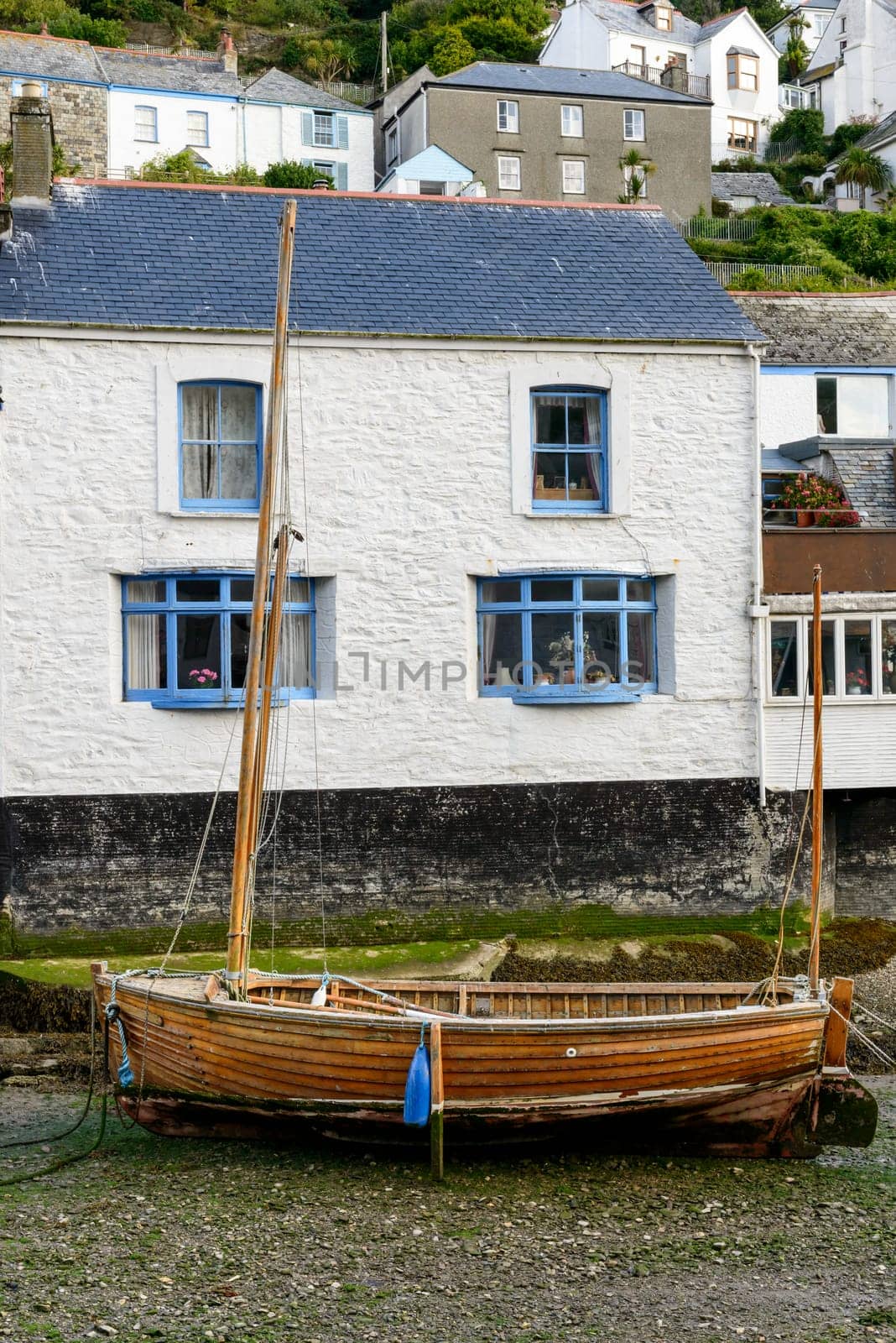 cityscape of the touristic village on southern coast of Cornwall with low tide in the river harbour and old wooden  boat aground.