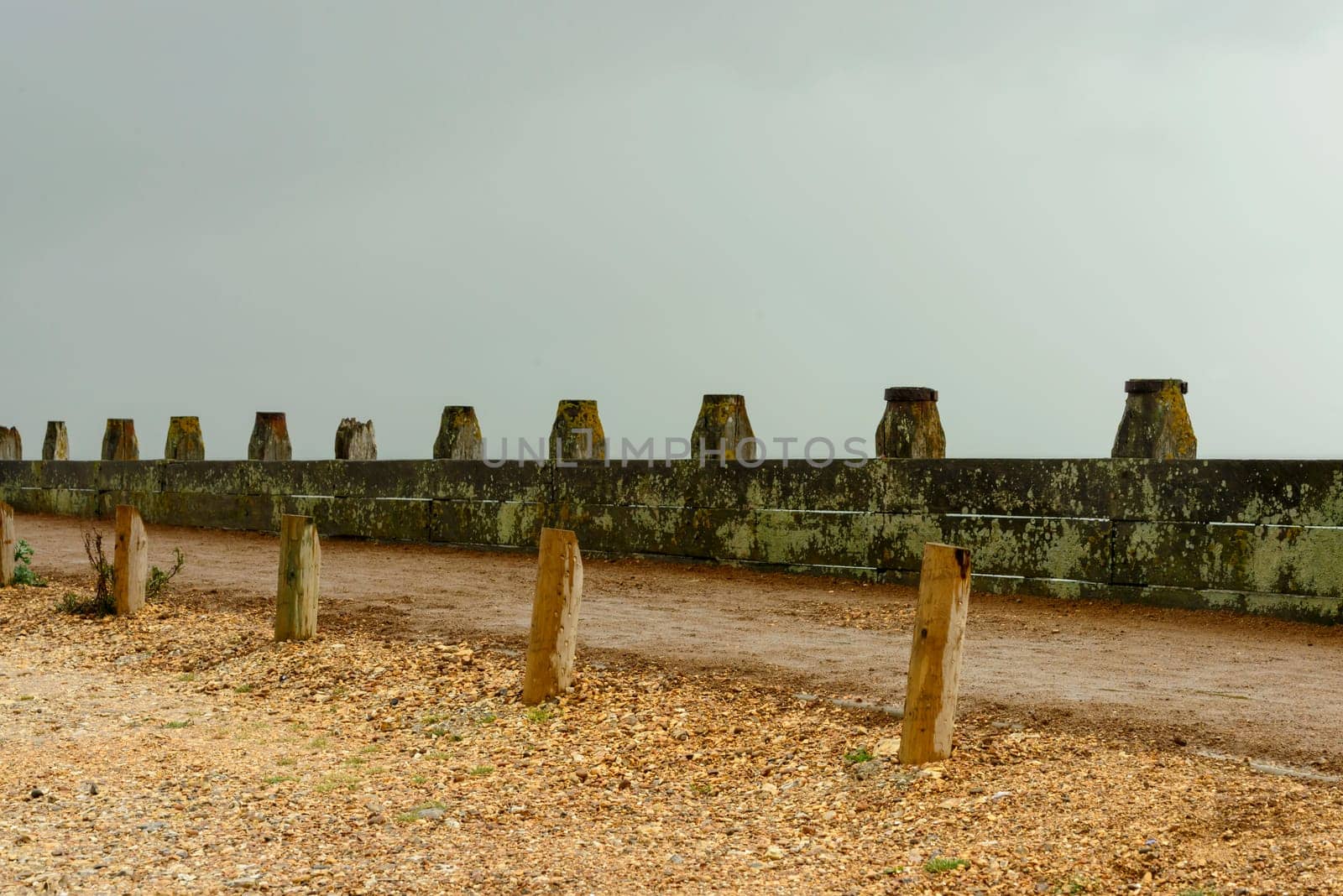 detail of foot path delimitattion at shingle beach of touristic location, shot under bright cloudy sky.