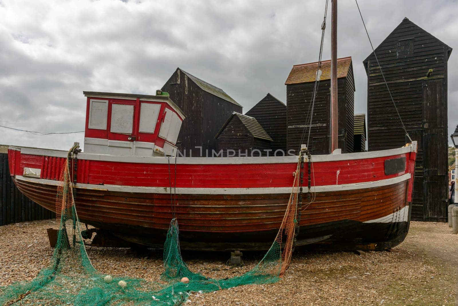 view of old fish boat amid fish net huts built in wood and painted black in historic village of Hastings, East Sussex .