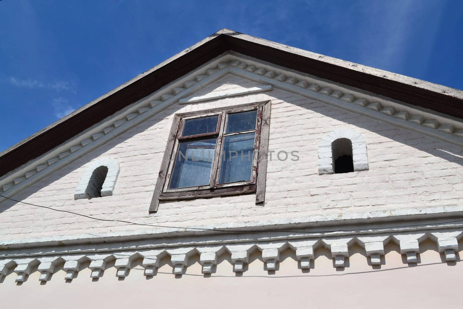 Attic window vent on old white brick, old house in Belarus, with blue sky background