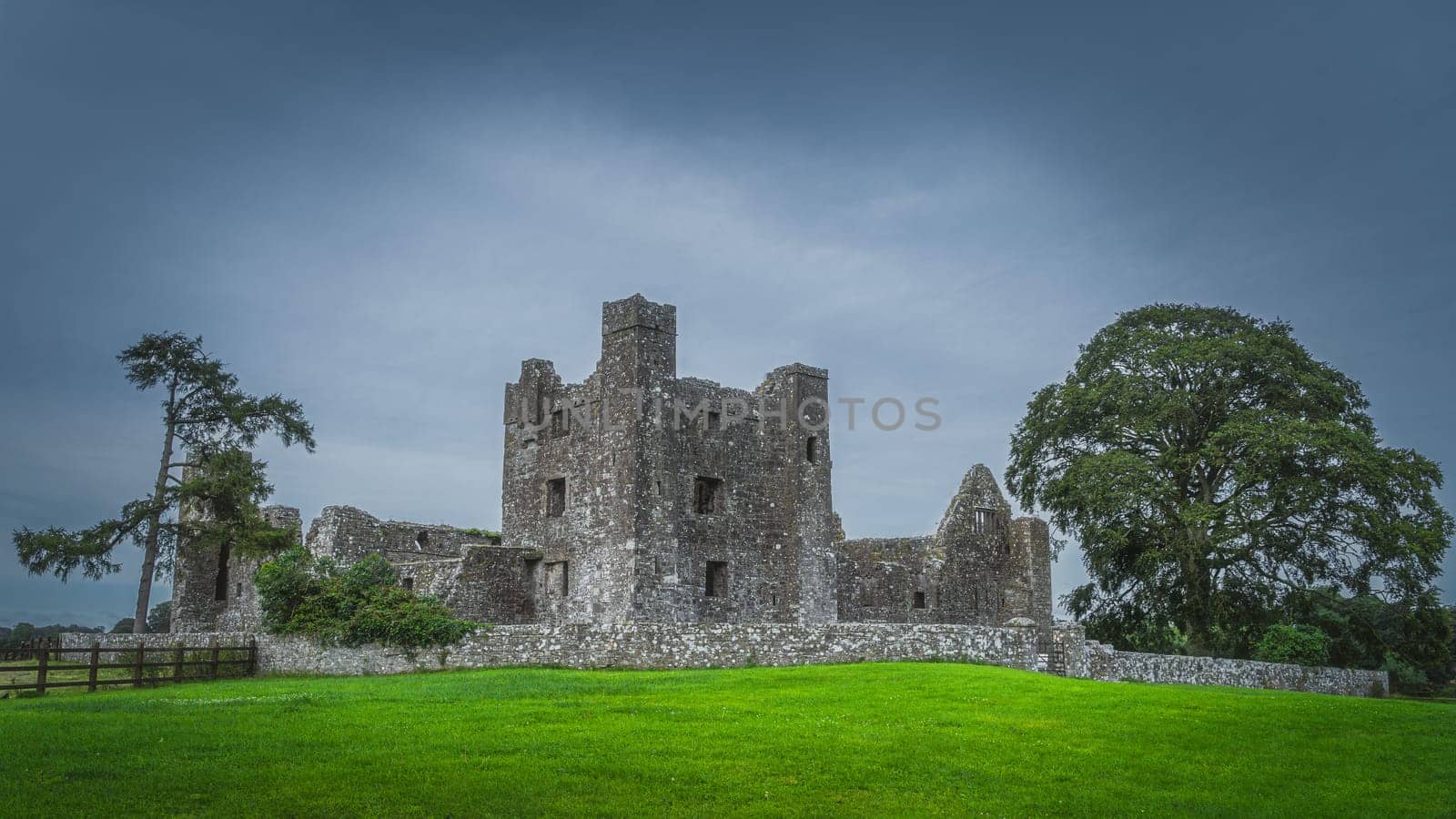 Beautiful old ruins of christian Bective Abbey from 12th century with green trees, pasture and moody dark sky in the background, County Meath, Ireland