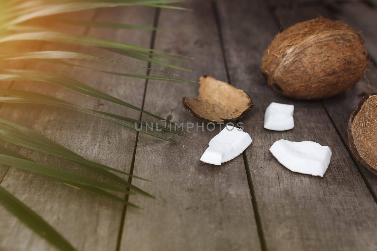 Broken coconuts on gray wooden background with palm leaf. White coconut pulp. High quality photo