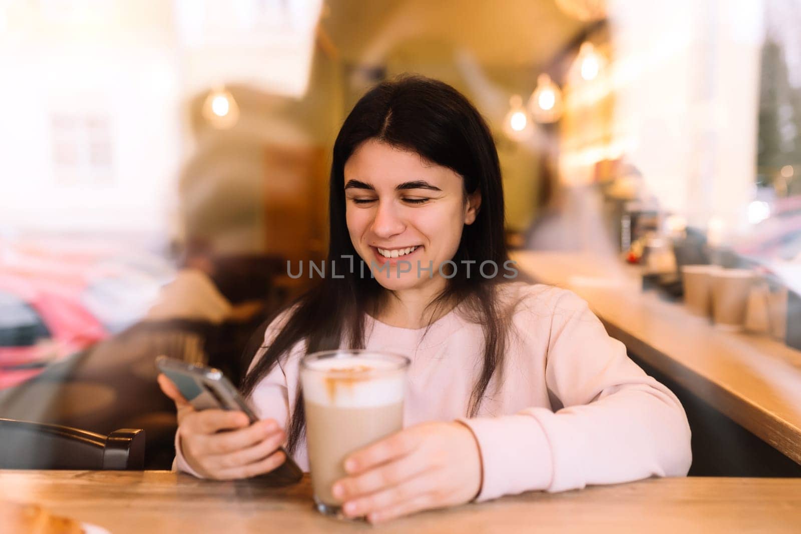 Girl smiling, drinks coffee in cafe and reading phone. Blurred background. High quality photo