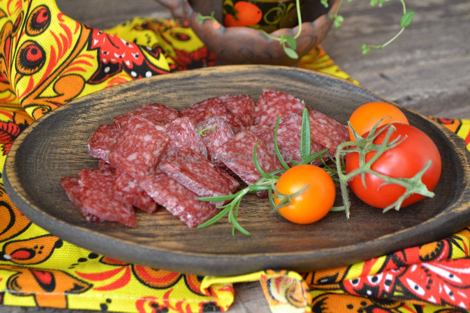 Salami sausages sliced on wooden rustic plate with tomatoes and rosemary