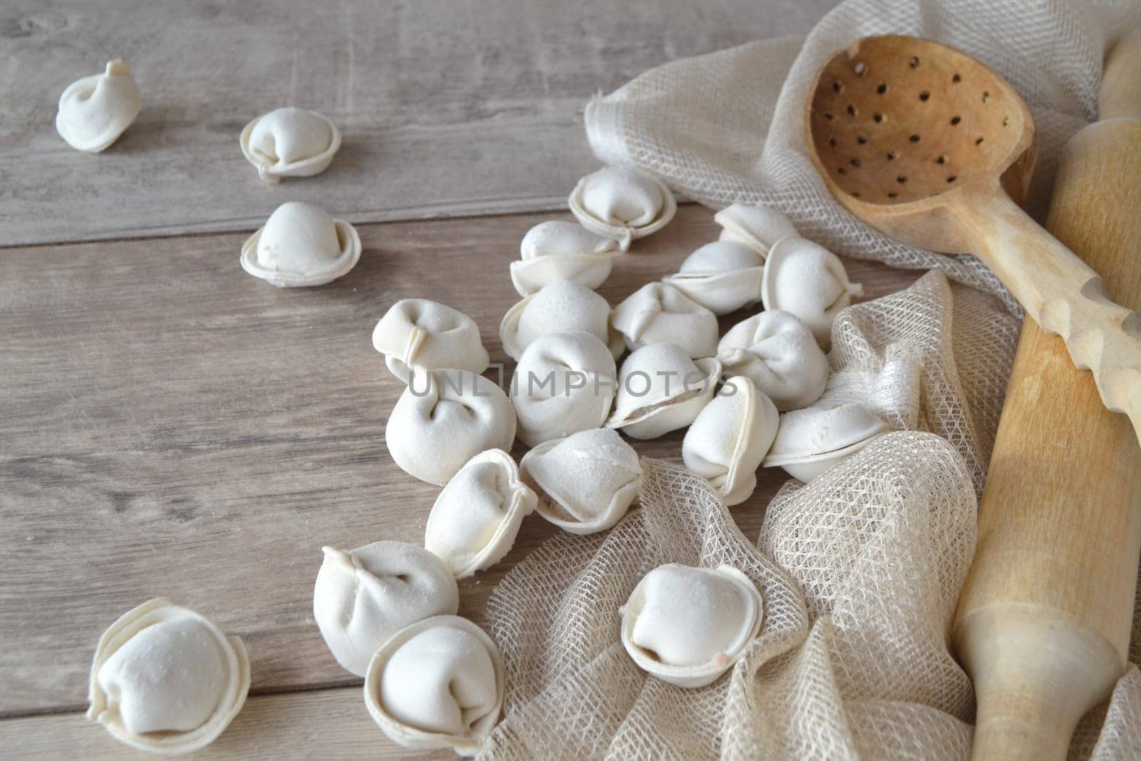 Homemade raw dumplings with flour on a wooden white table.