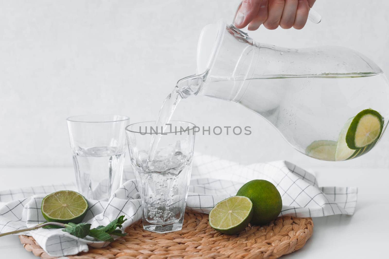 Detox water with lime fruit. Hand pouring lime fruit water from jug into glasses.