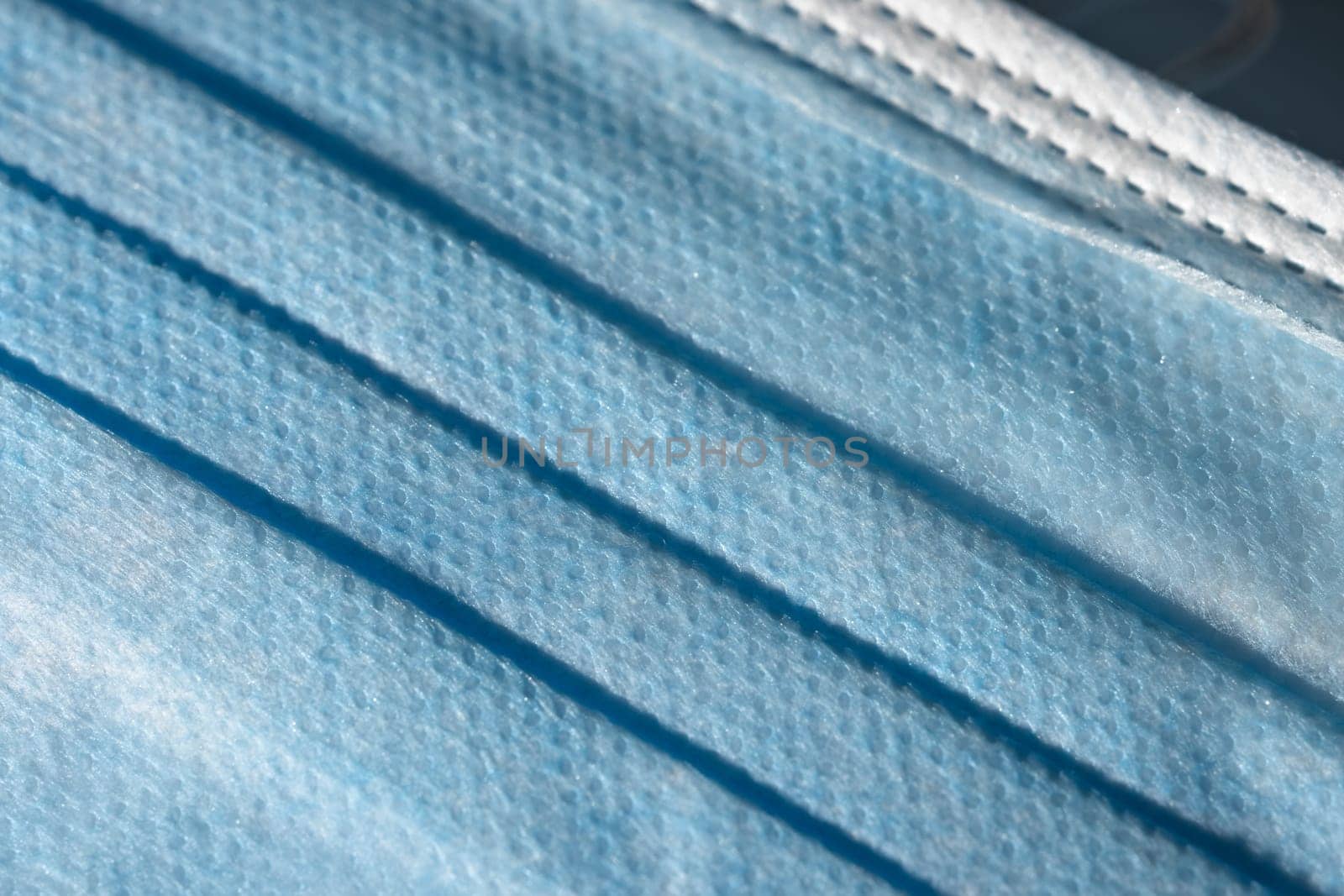 Close up of the front blue surface of a medical or surgical face mask. Man made single use item of Personal protective equipment, plastic texture.