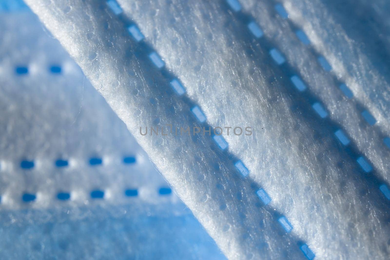 Super macro abstract close up of a 3-ply disposable face mask. Individual fibers visible along the printed paper like seam. Background with copy space