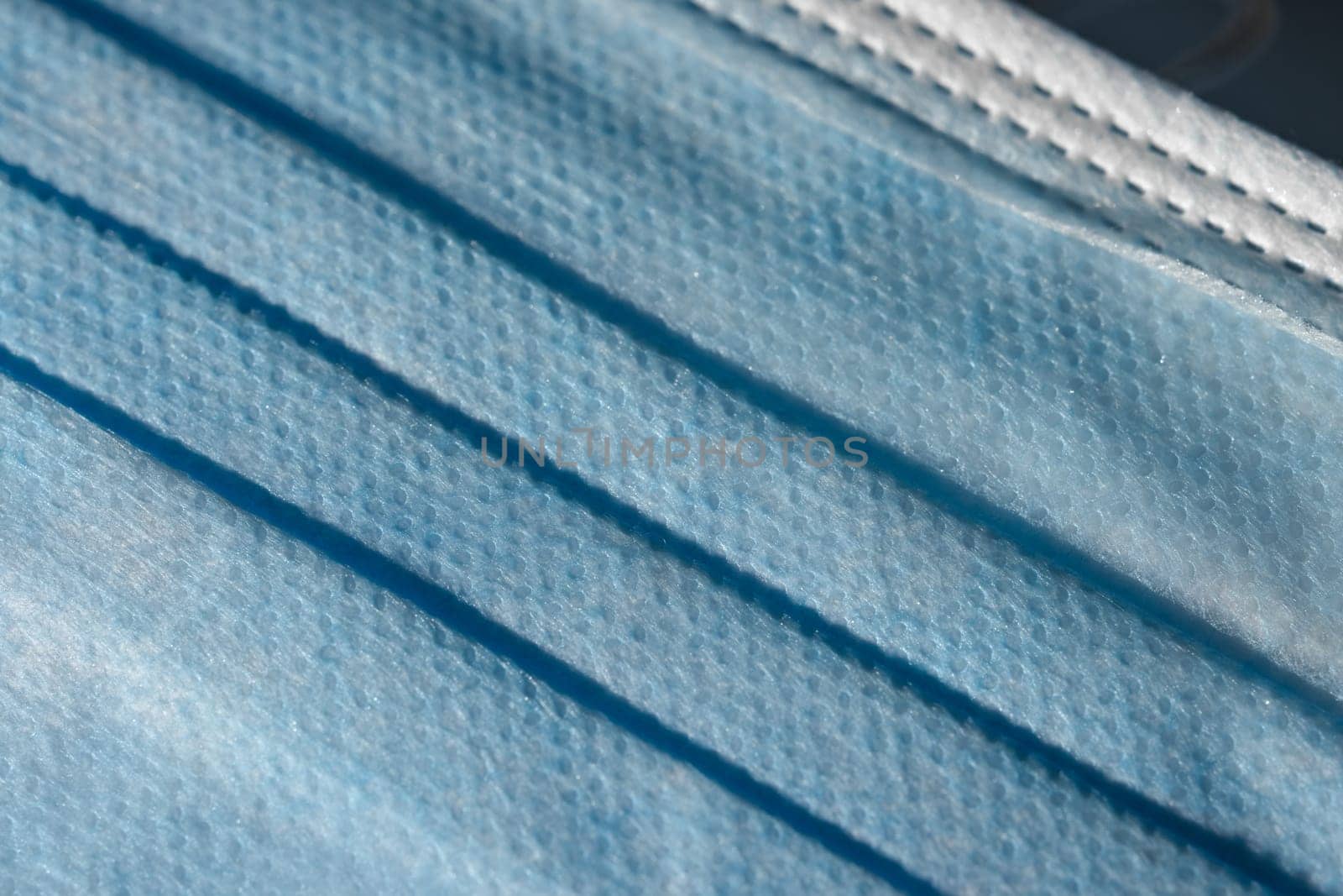 Blue dimpled texture and folds of a disposable 3-ply medical face mask. Mandatory use for many people in public spaces due to Covid aka coronavirus.