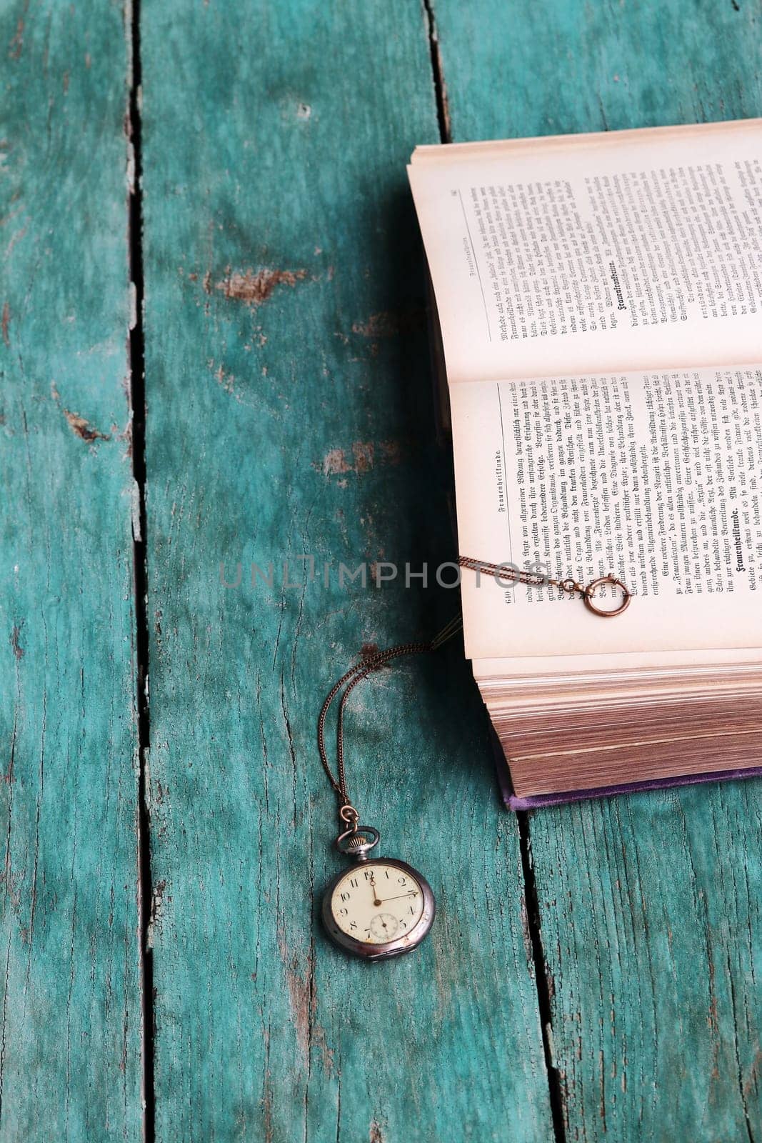 An antique pocket watch and an old book on a blue wooden floor