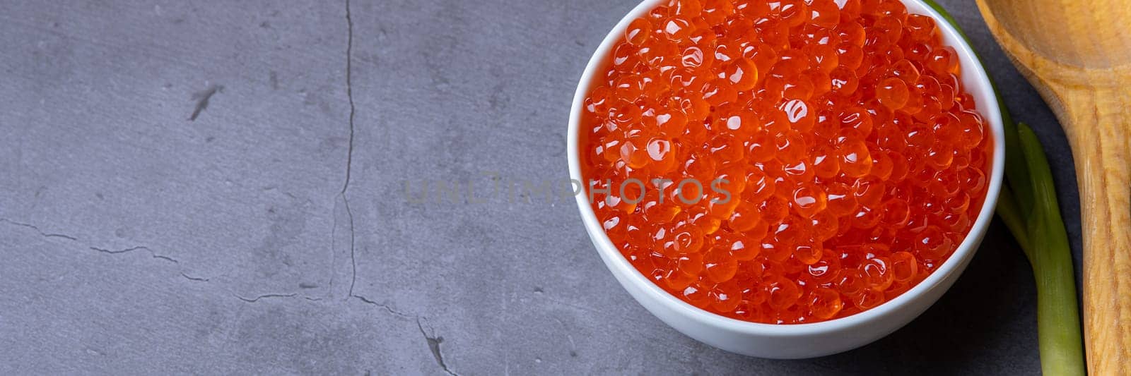 Red caviar in a wooden cup on a grey background with a spoon. Place for advertisement, logo, label, mockup, mock-up.