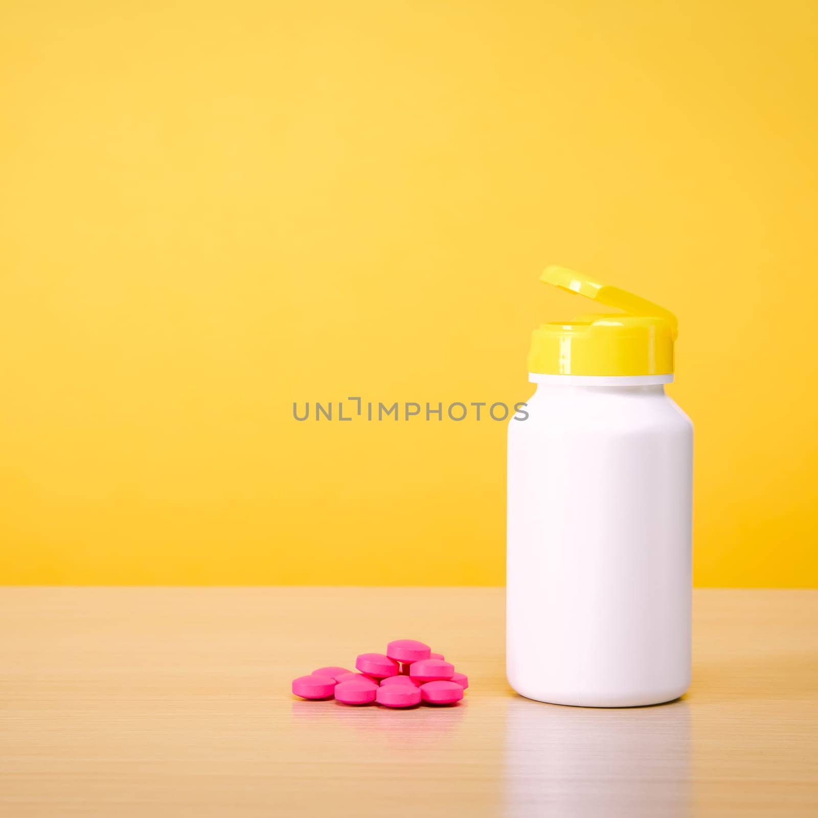 A white jar with scattered red pills on a yellow background. Place for the label, logo, layout.