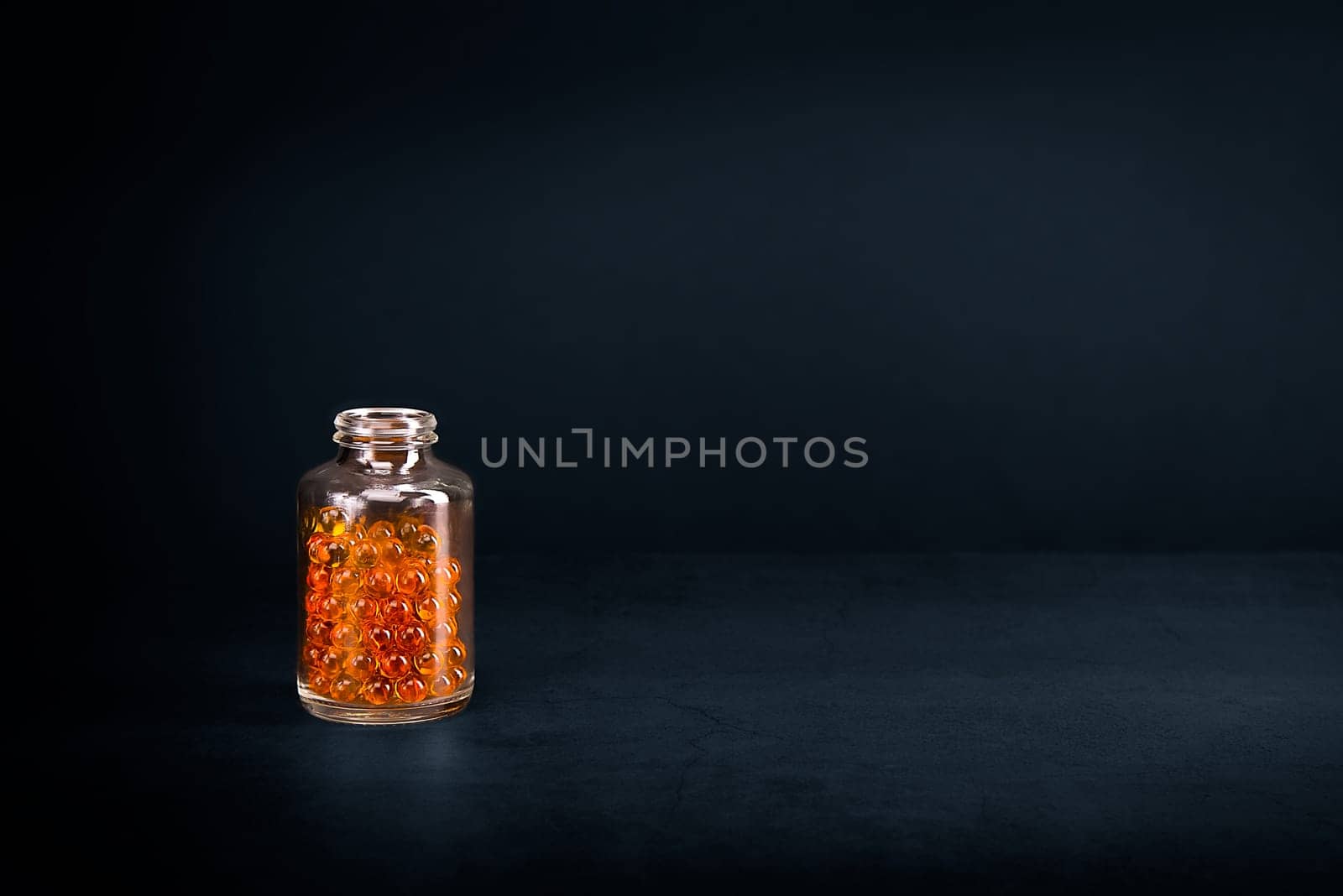 A glass jar with pills of bright orange yellow color on a blue background. Place for the label, logo, layout.