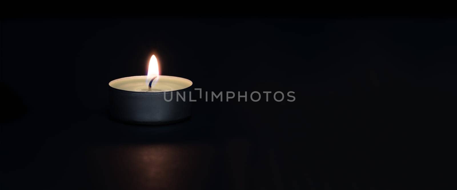 A burning candle on a dark background with a flare in the foreground. Layout, mockup.