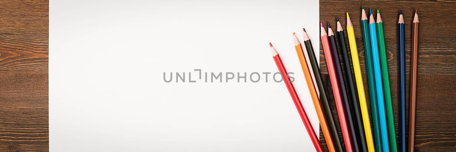 The sheet is pure white and colored pencils for drawing on a wooden background with a place to copy. Mock-up, mockup, layout.