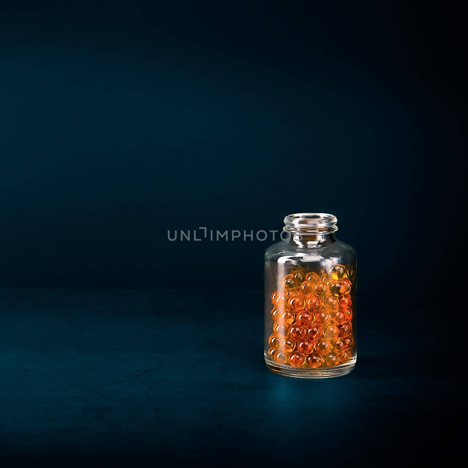 A glass jar with pills of bright orange yellow color on a blue background. Place for the label, logo, layout.