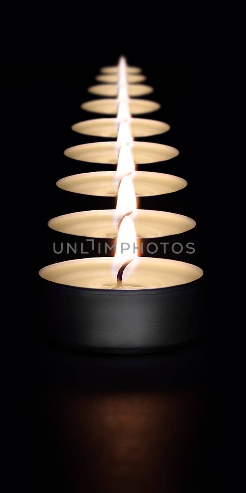 A row of burning candles on a dark background with a flare in the foreground. Layout, mockup.