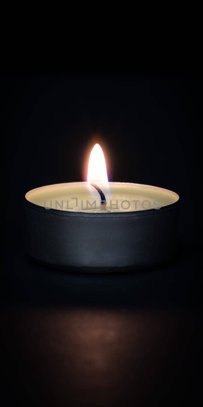 A burning candle on a dark background with a flare in the foreground. Layout, mockup.