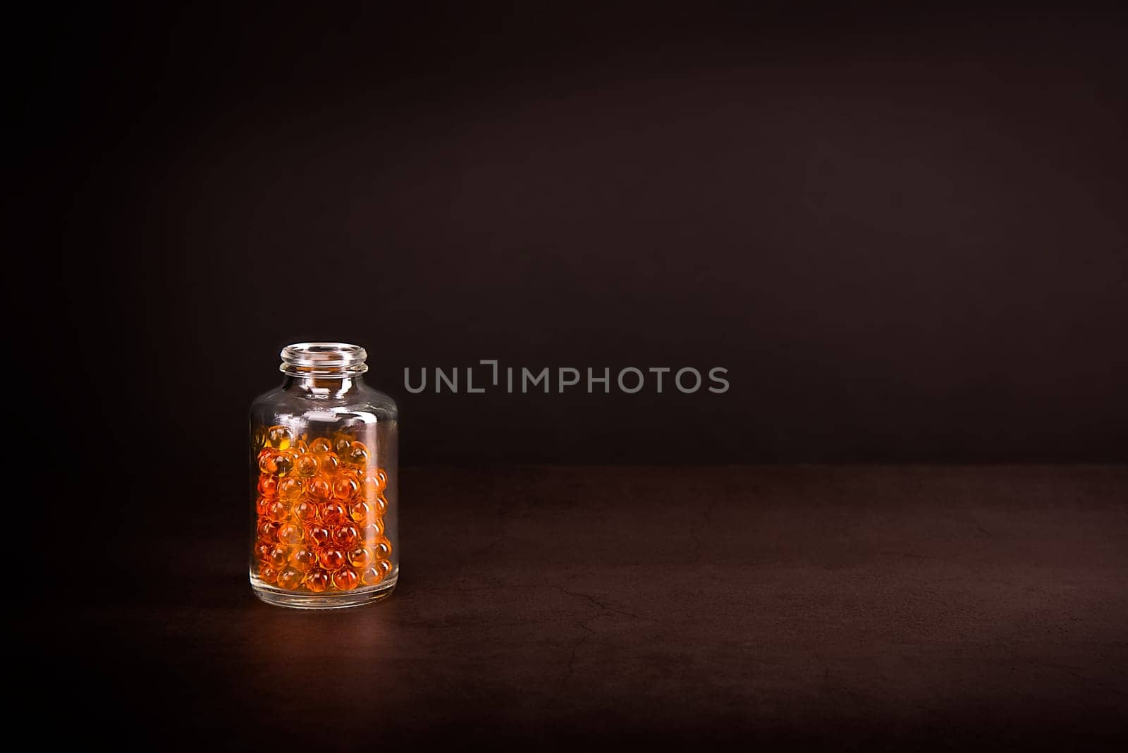 A glass jar with pills of bright orange yellow color on a brown background. Place for the label, logo, layout.
