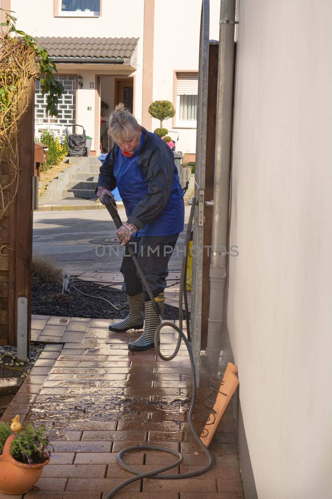 Woman cleaning terrace with a power washer - high water pressure cleaner on wooden terrace surface