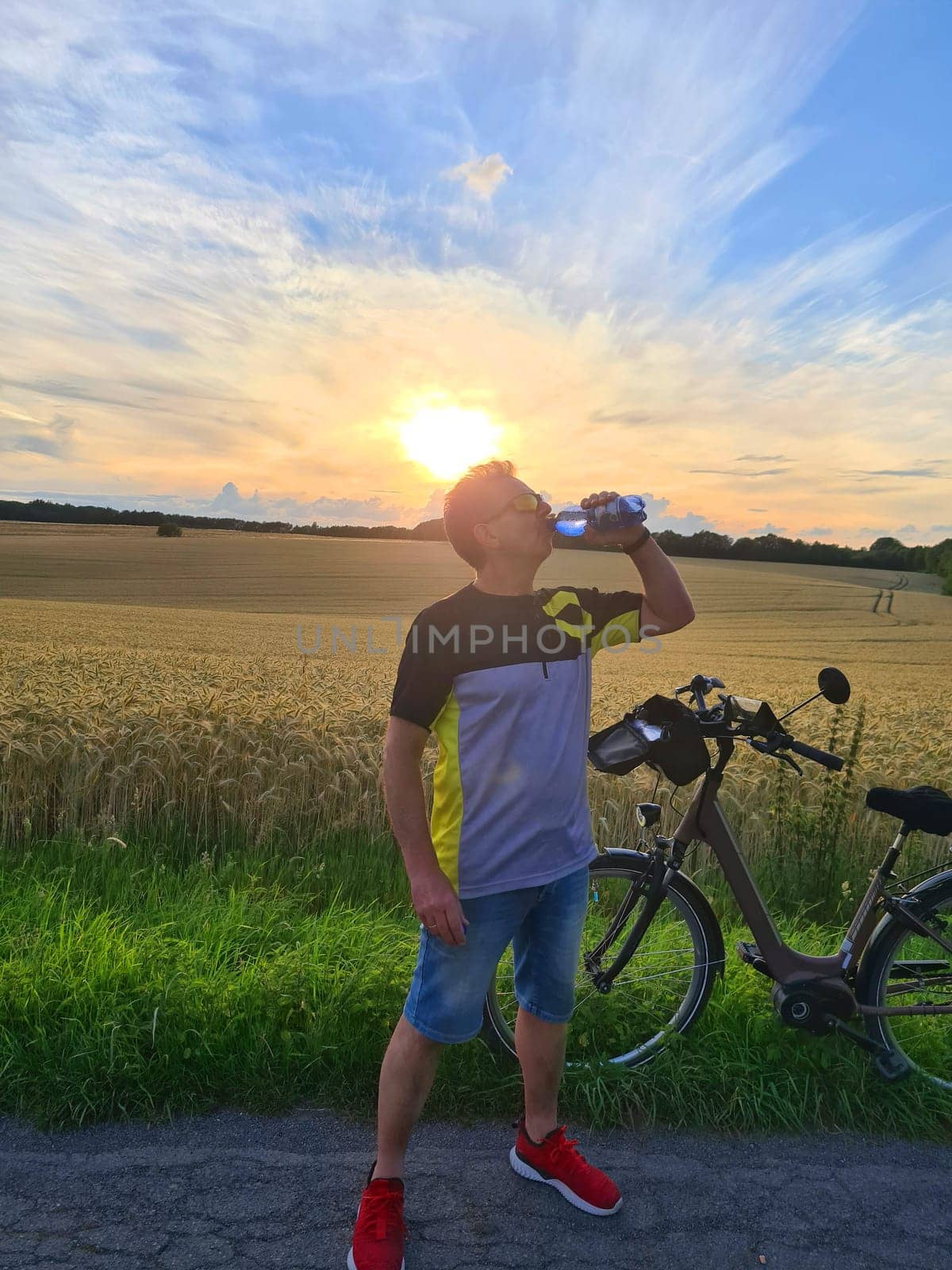 Handsome young professional cyclist dressed in cycling clothing and protective helmet feeling free and happy, drinking water from the bottle, enjoying bicycle in warm spring. Recreation of sportsman.