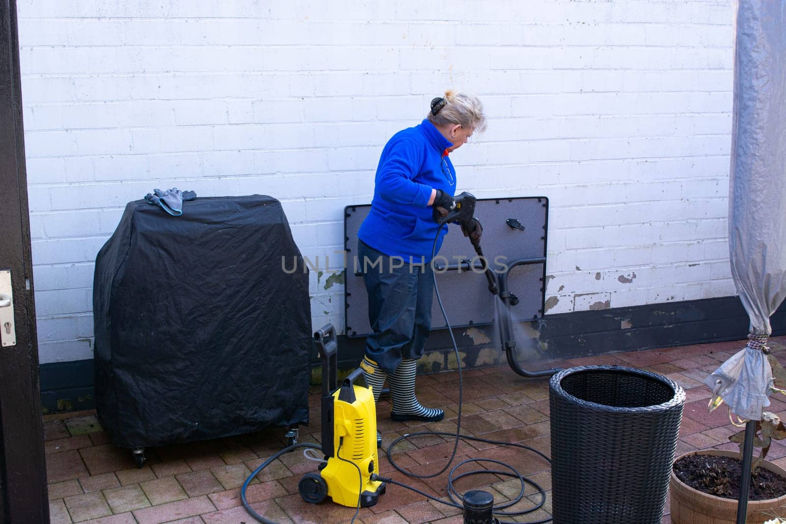 Woman cleaning terrace with a power washer - high water pressure cleaner on wooden terrace surface