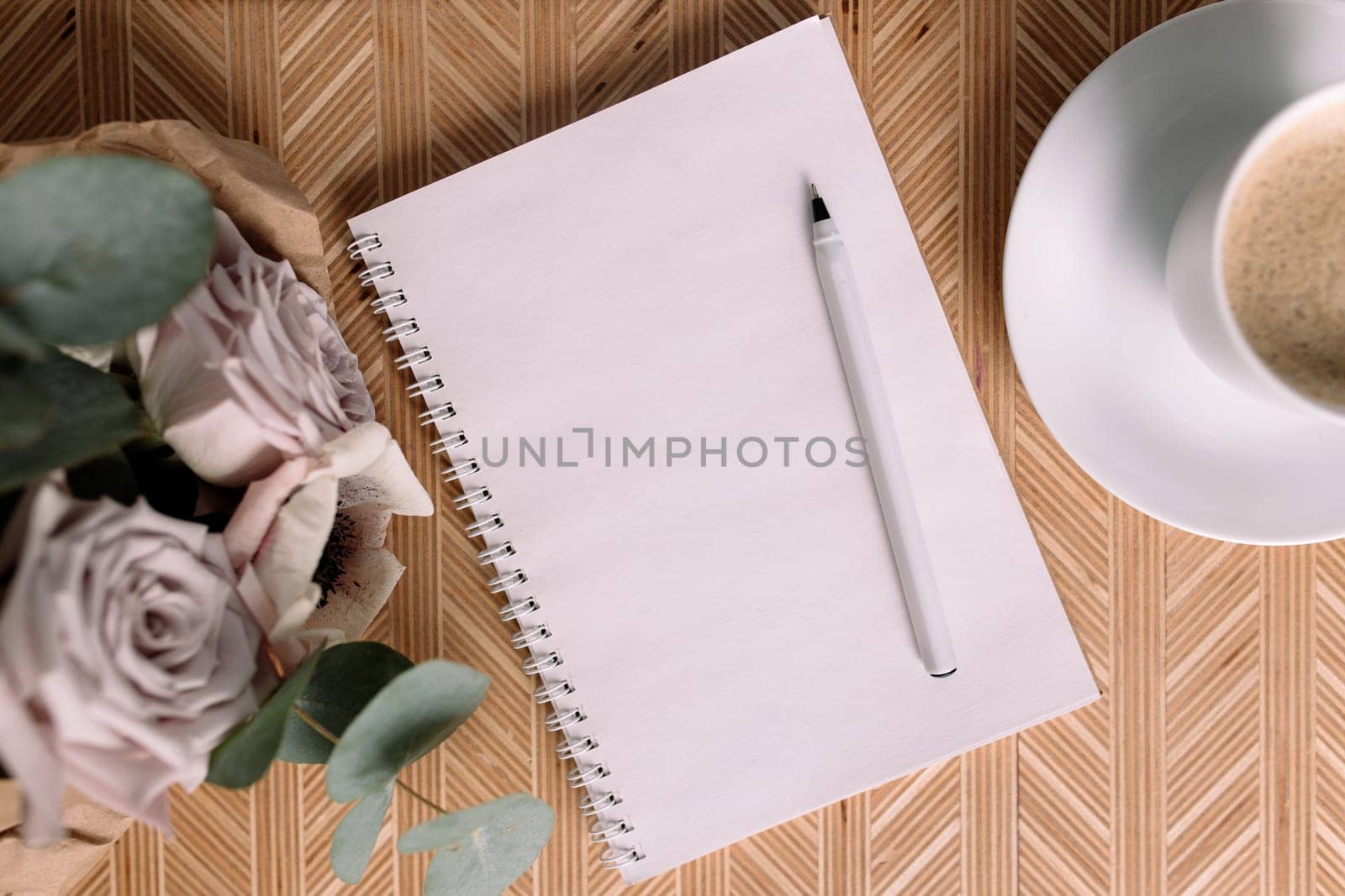 Romantic morning. Wooden coffee table with flowers on bed flat lay, coffee cup, flowers, note pad, pen. Lilac roses with eucalyptus and anemones. High quality photo