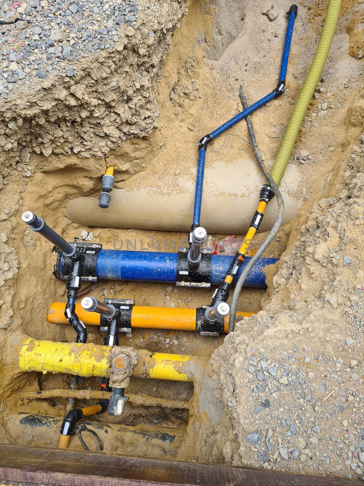 Work on the installation of engineering and heating systems. Two plastic pipes one yellow for gas pipe and one black for power lines. They are in a sand ditch.