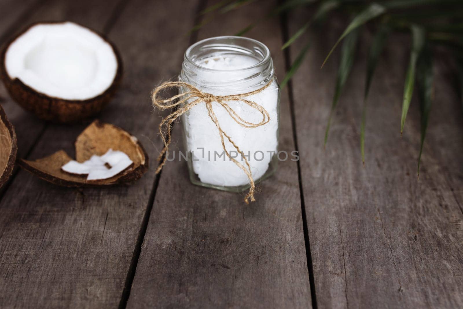 Broken coconuts on gray wooden background with jar of raw organic extra virgin coconut oil and palm leaf. White coconut pulp. High quality photo