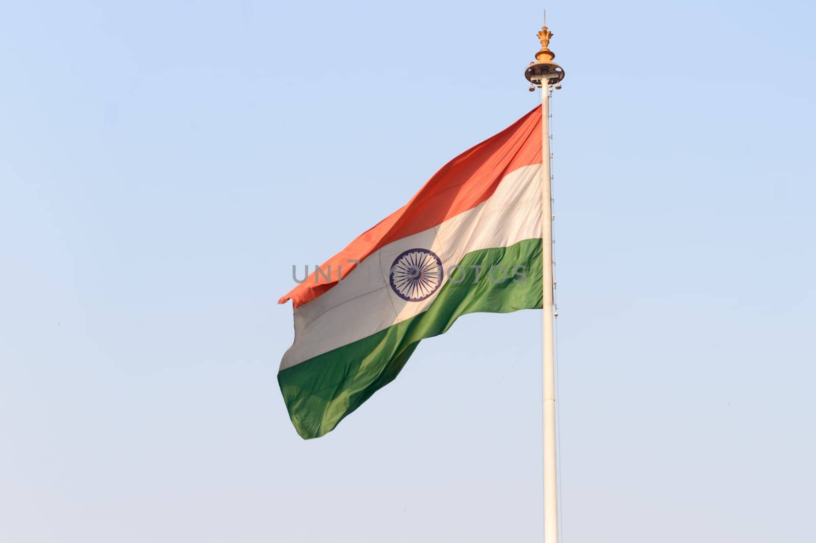 Indian flag flying against blue sky background. The National Flag of India is a horizontal rectangular tricolor (saffron, white and green color) with the Ashoka Chakra at its center.