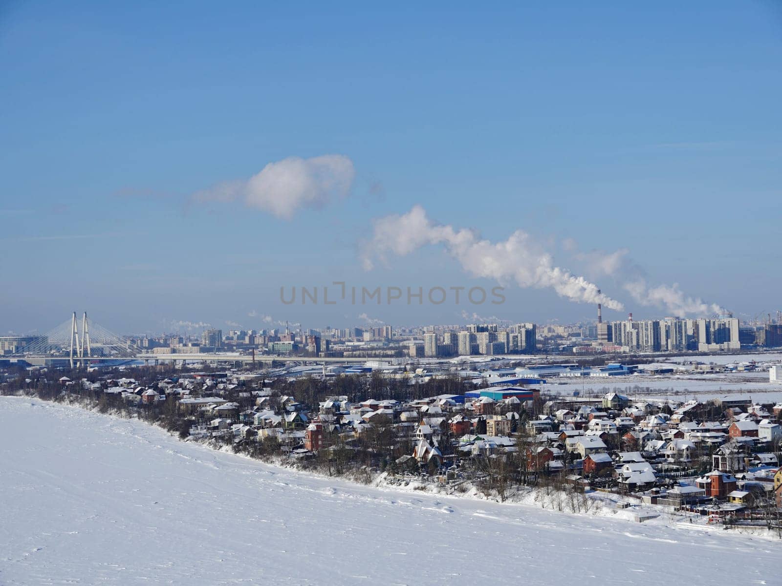 Bird's eye view of a suburban village on the banks of a river in winter, a river and small houses under the snow, a cozy calm suburban life in nature