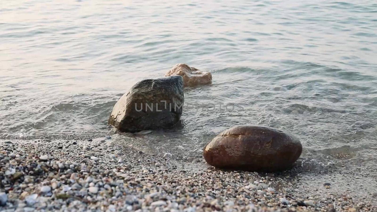 Lake water hits shore rocks. Transparent waters of Lake Garda located in northern Italy, a tourist destination of excellence.