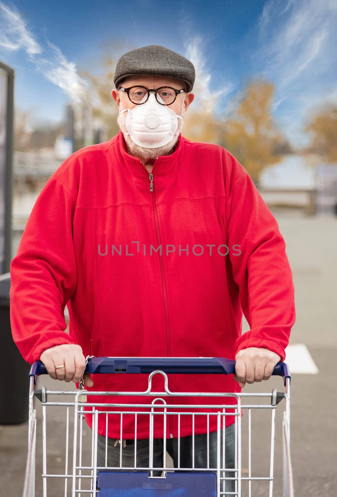 A senior man wears an N95 respirator mask while pushing a shopping cart outside of a grocery store. The man is protecting himself from coronavirus and other airborne particles and diseases.