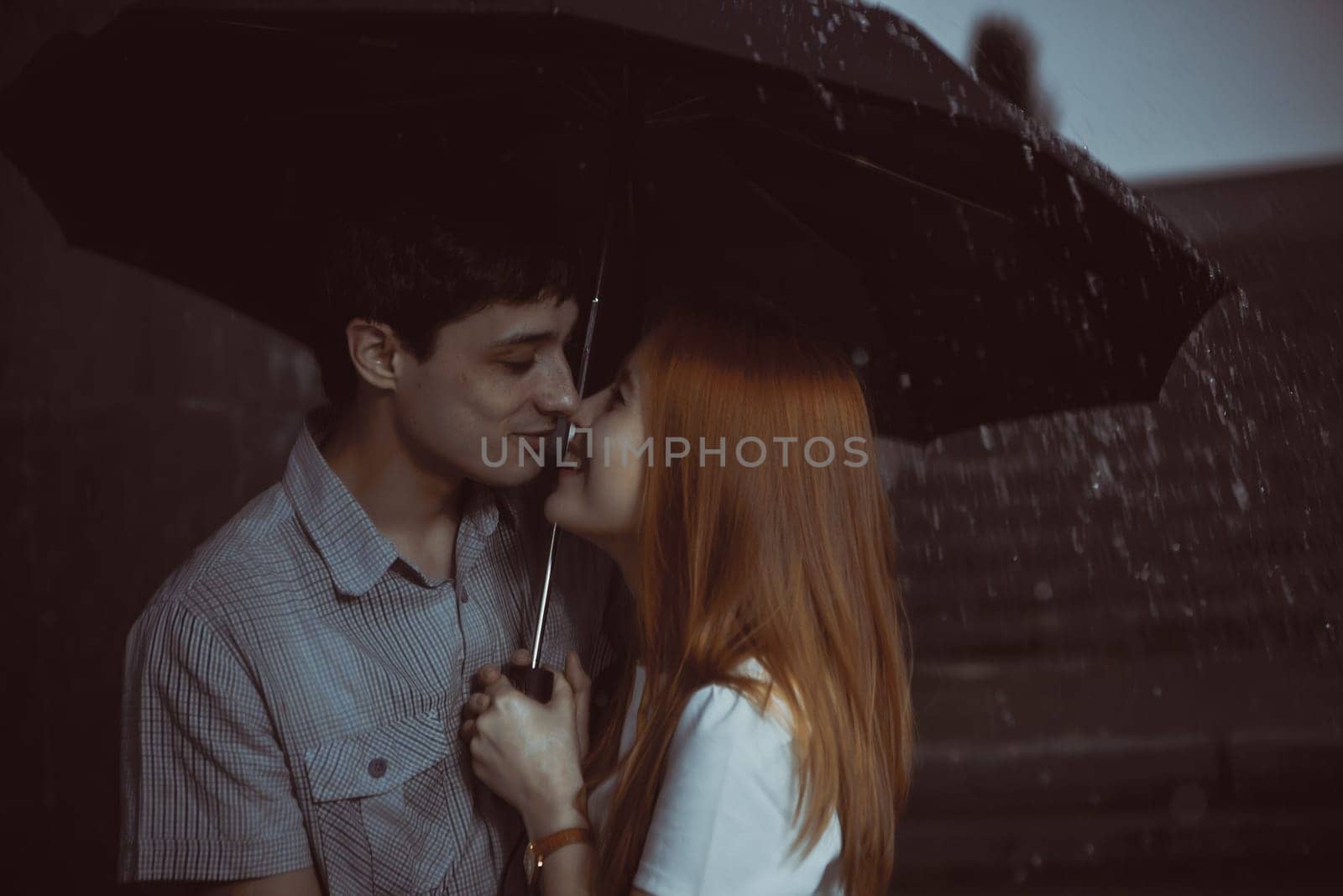 Man and the girl kiss in the rain. Photo contains glare from lights.