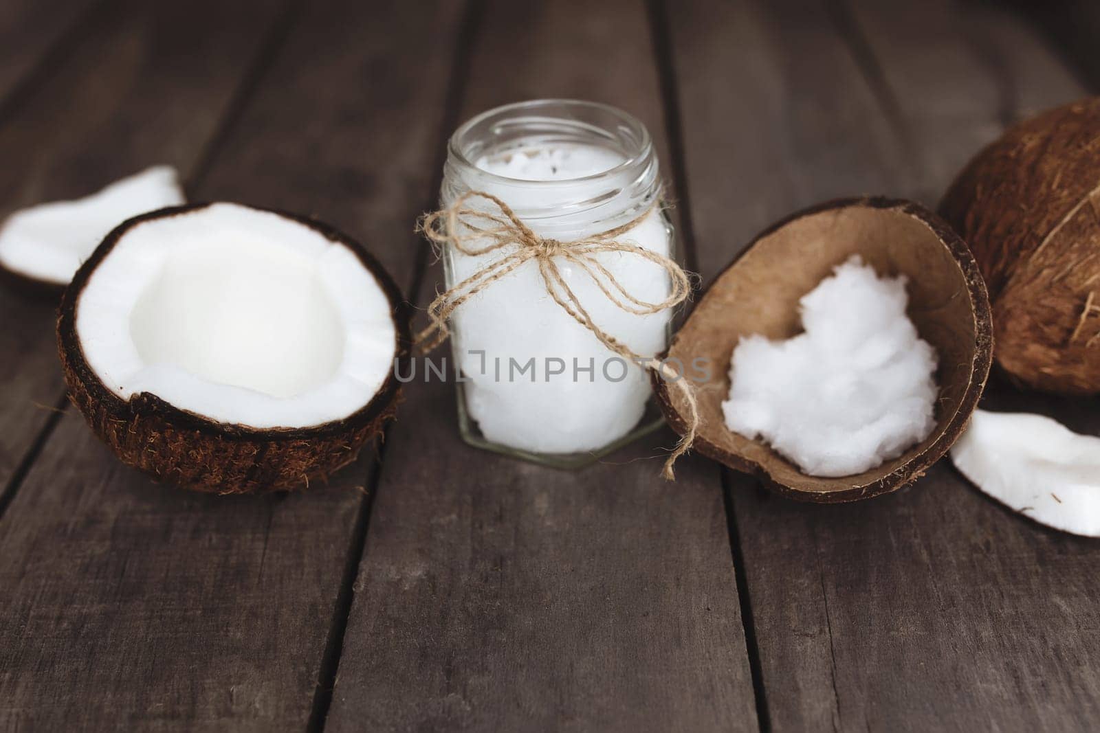 Broken coconuts on gray wooden background with jar of raw organic extra virgin coconut oil. White coconut pulp. High quality photo