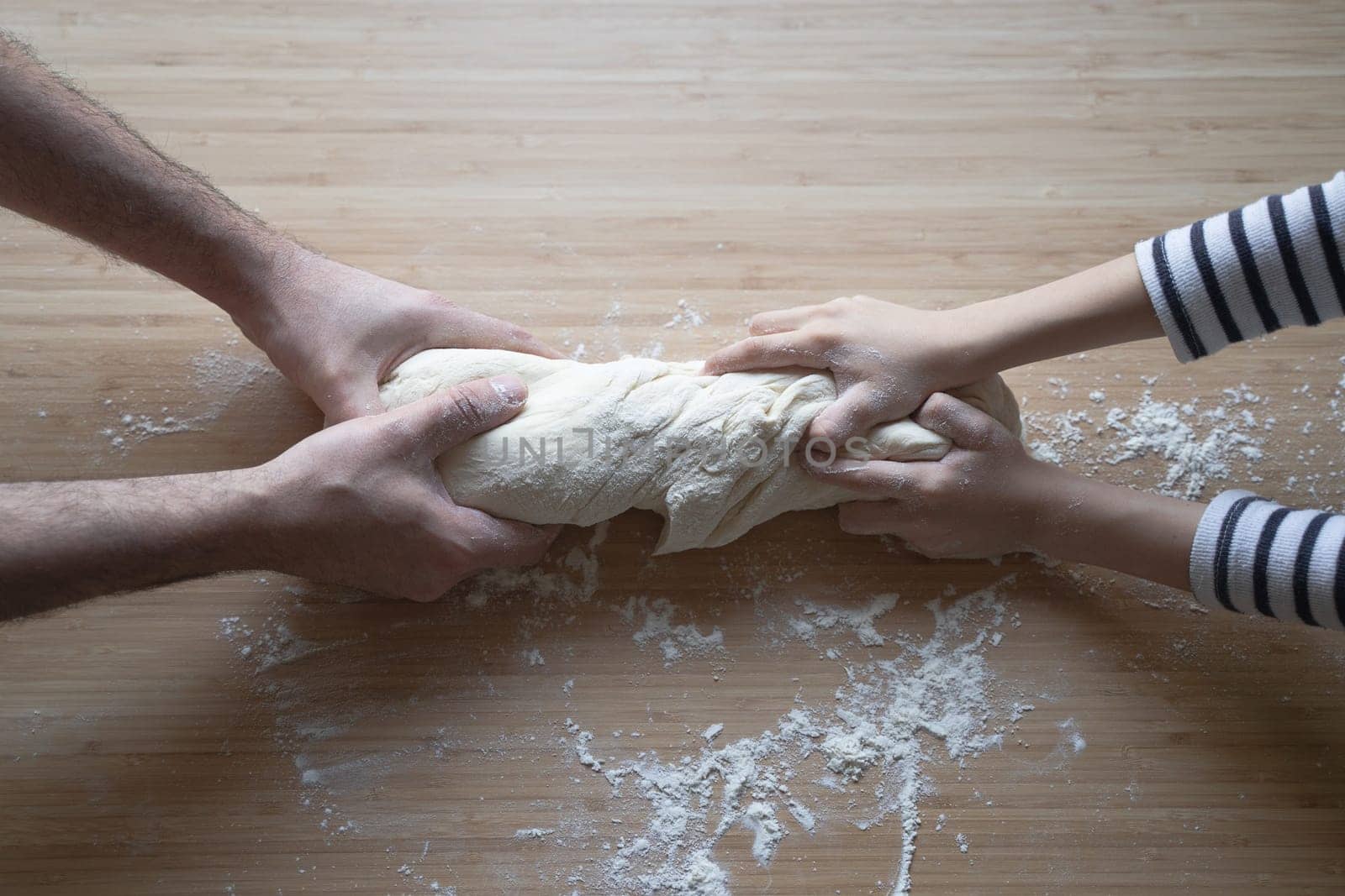 side view close up portrait of Caucasian child hands working the dough at home with his father on a kitchen wood cutting board in natural window light