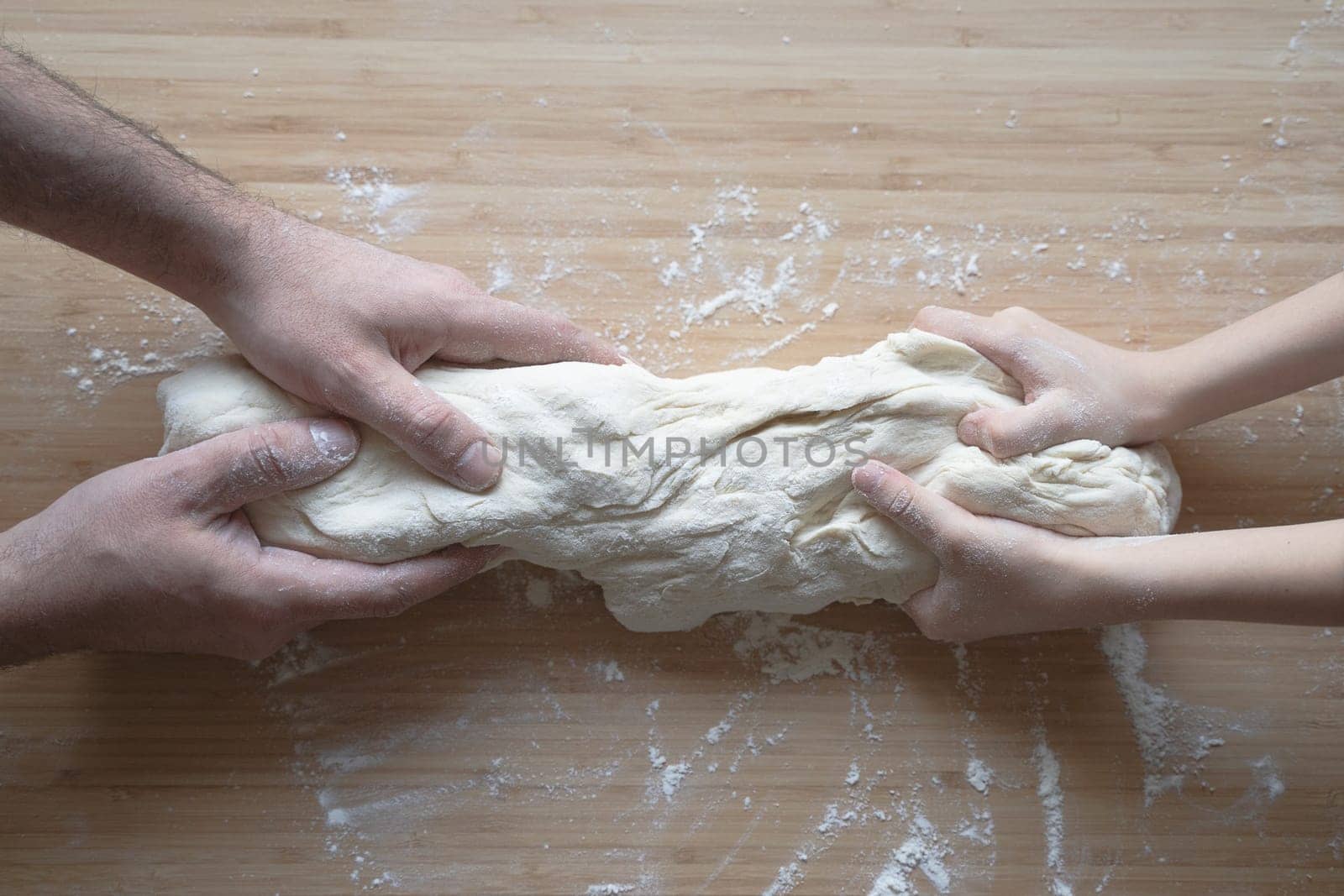side view close up portrait of Caucasian child hands working the dough at home with his father on a kitchen wood cutting board in natural window light