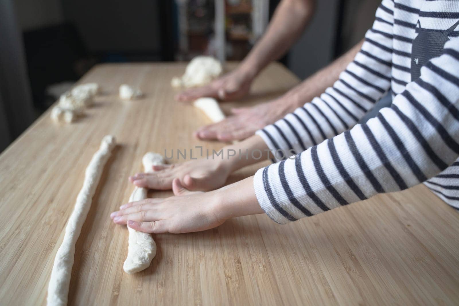 side view close up portrait of Caucasian child hands with stripped shirt working the dough at home with his father on a kitchen wood cutting board in natural window light