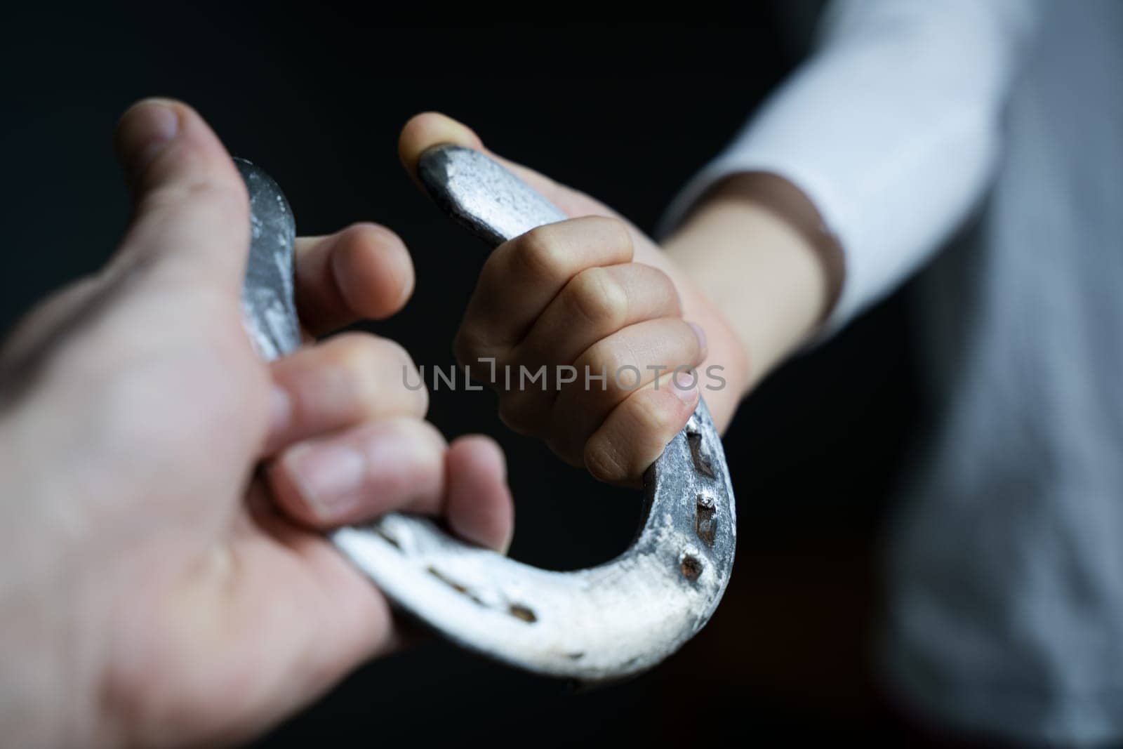 point of view of Caucasian male hand giving a child with white shirt a shiny steel polished horshoe in natural light