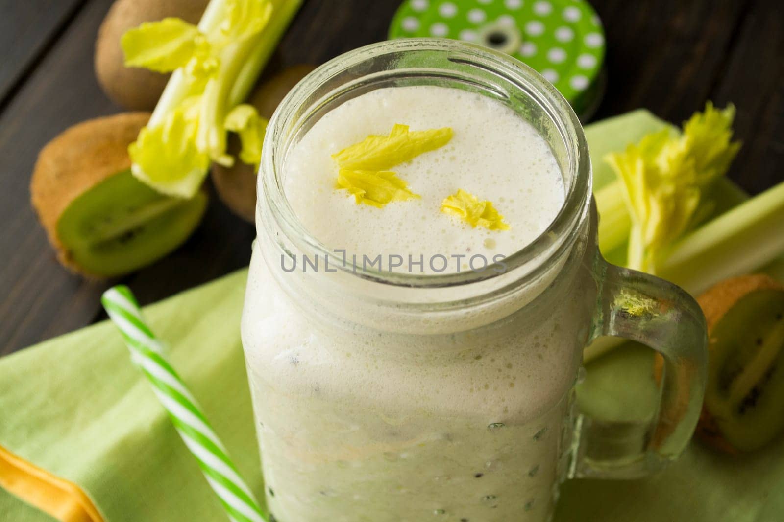 green smoothie in a glass jar with lid and a straw, celery and kiwi over dark wooden table