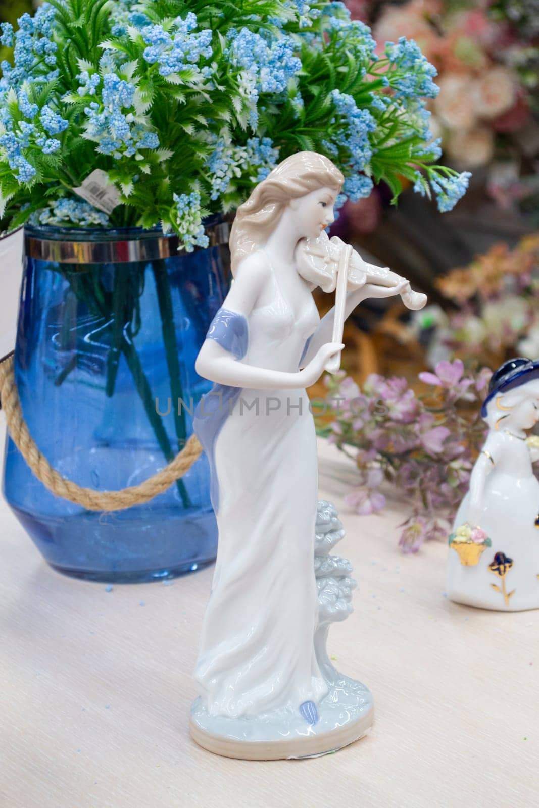 German porcelain figurine of a violinist girl. Ceramic figurine of the violoncellist in retro style with blue flowers in a vase on the table