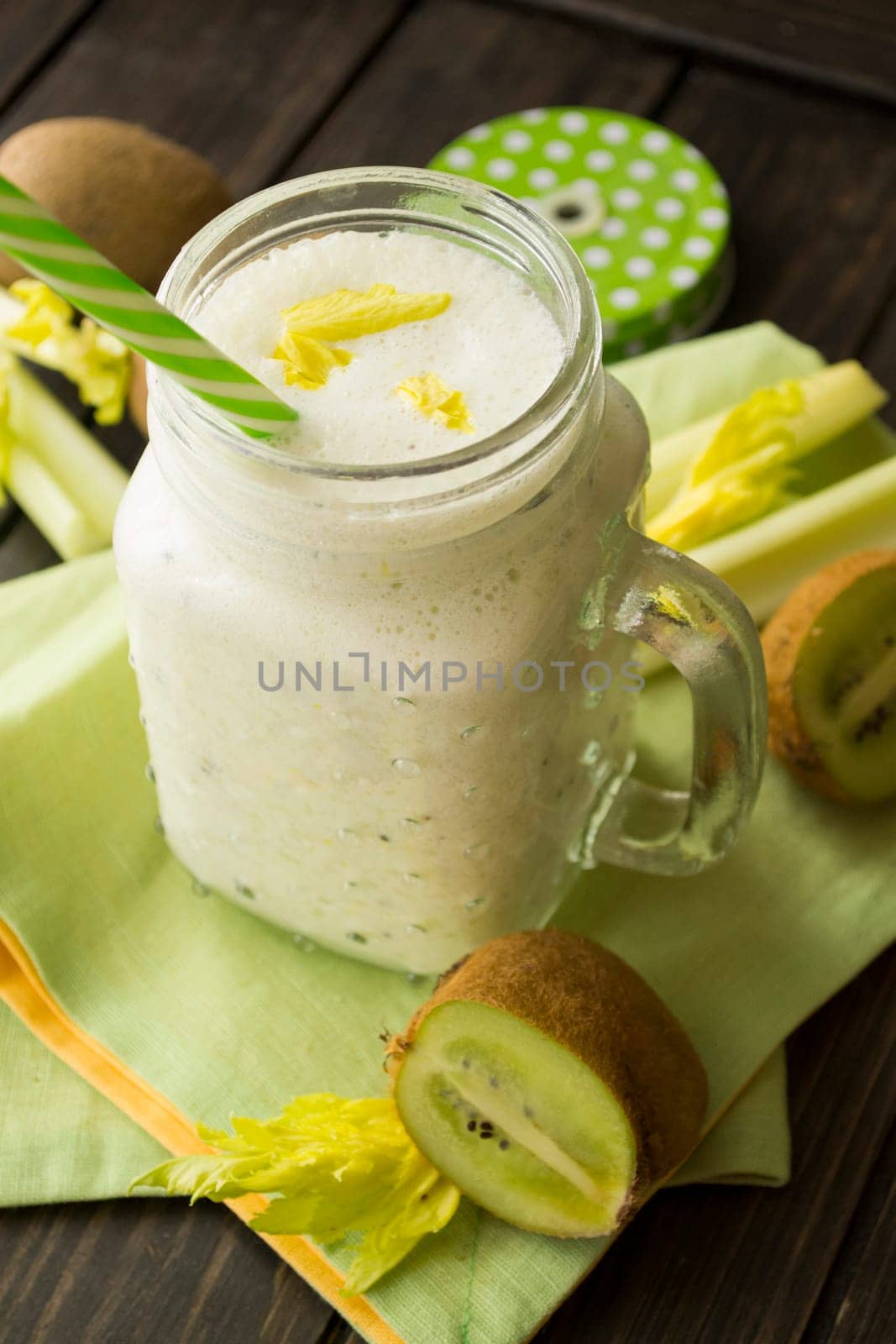 Blended green smoothie with ingredients celery and kiwi on wooden table, vertical image