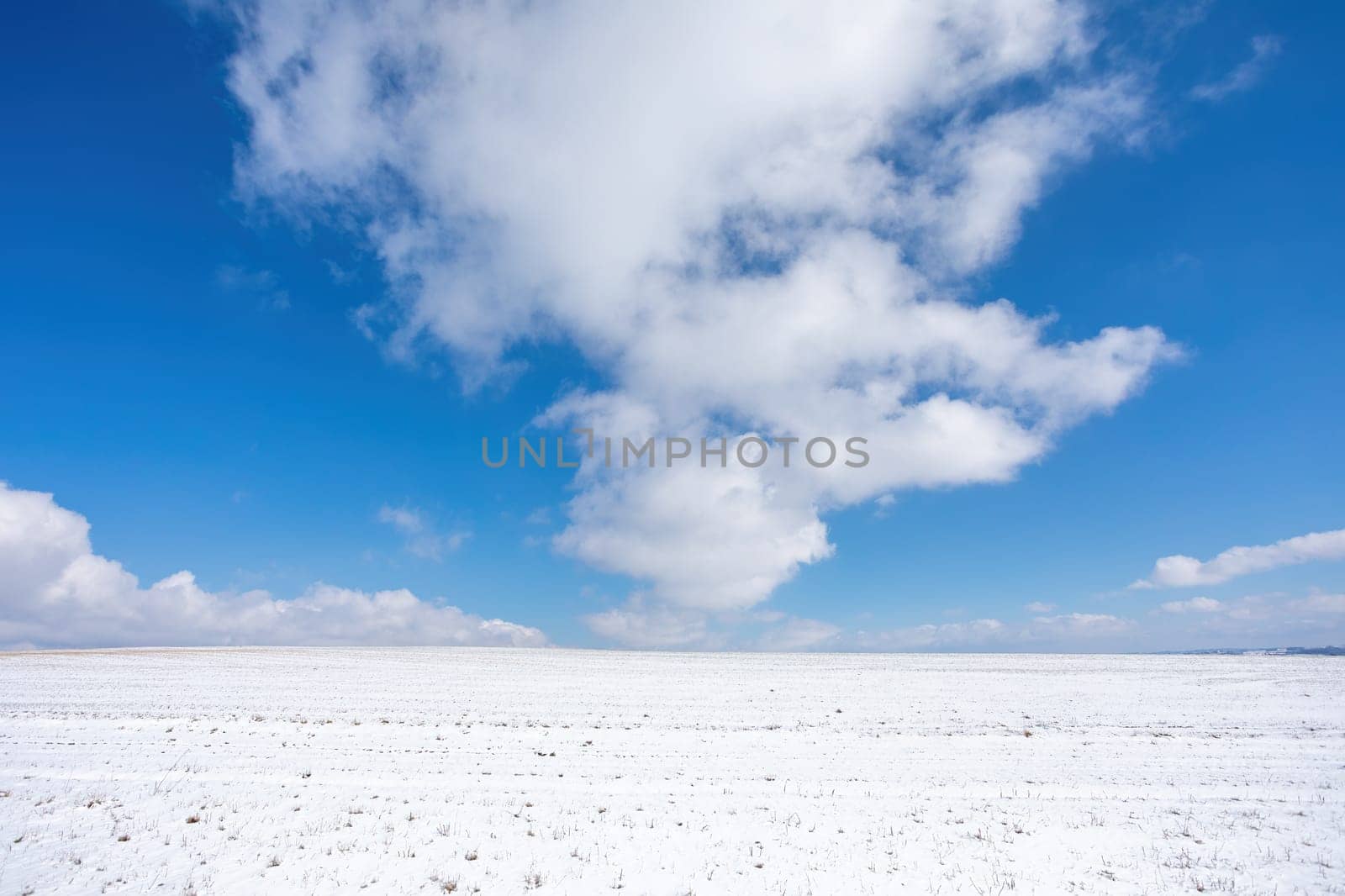 Simple winter background with beautiful lines from skier and big clouds on horizon with blue sky
