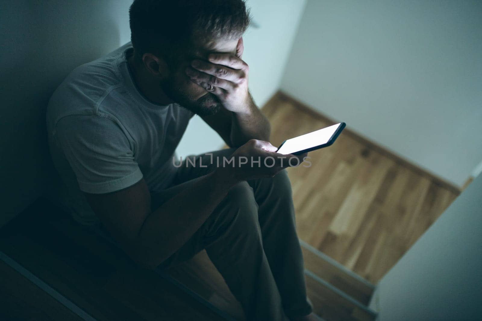 Depressed man sitting in the dark with his smartphone