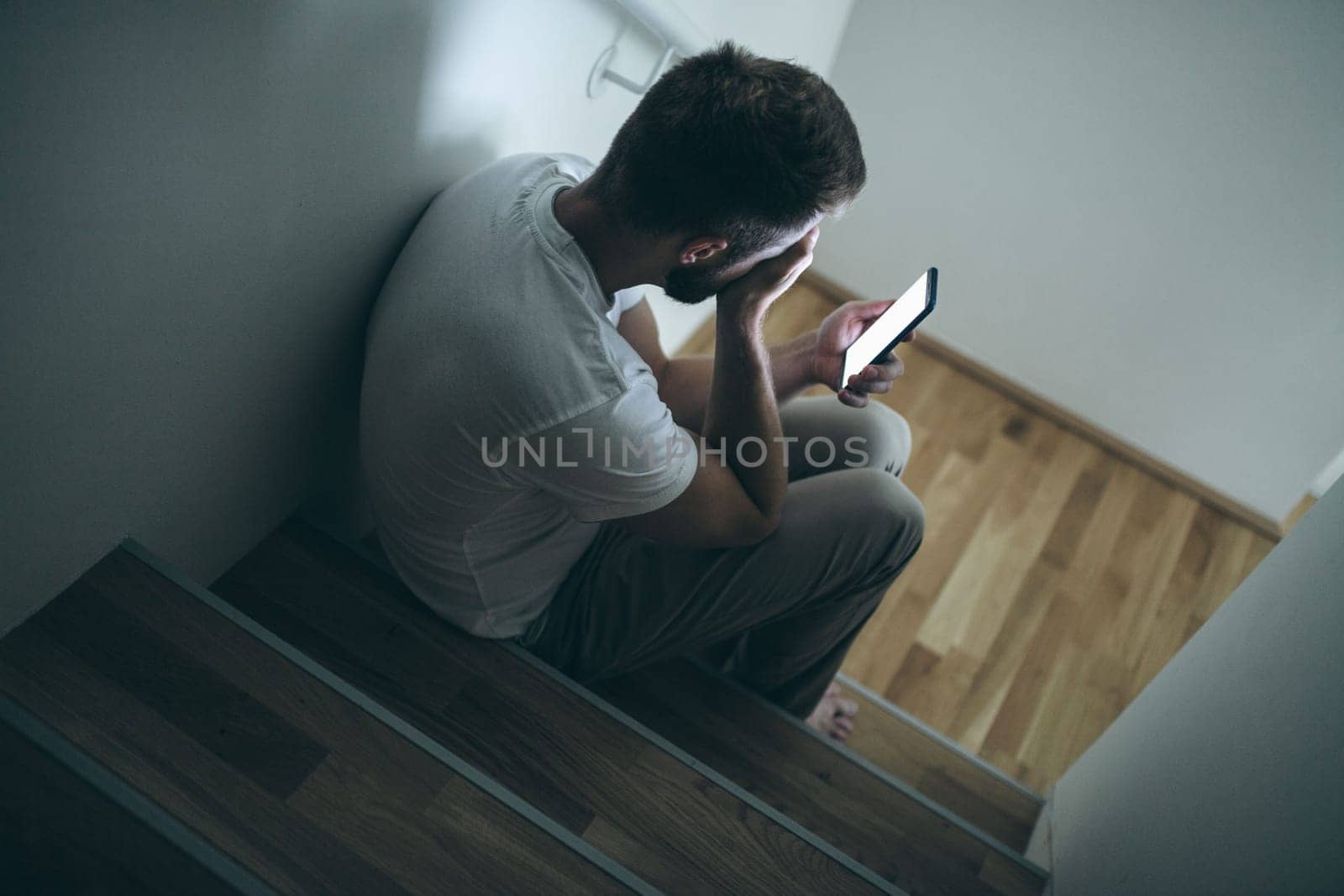 Depressed man sitting in the dark with his smartphone