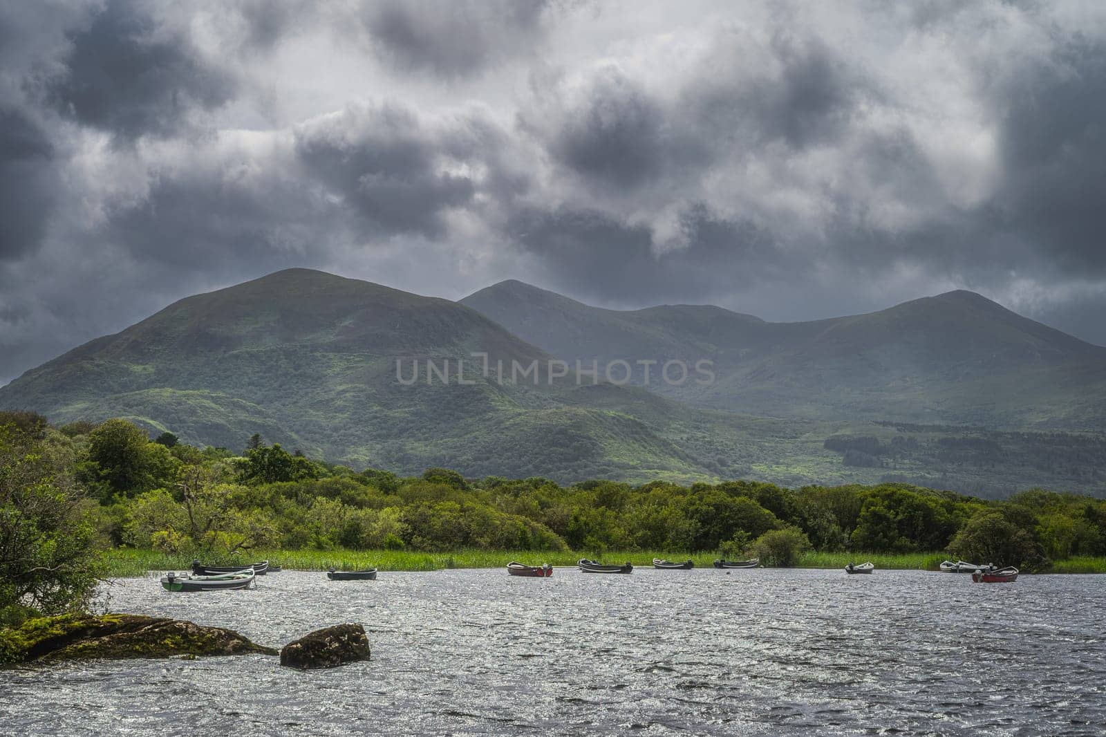 Wooden boats moored on Lough Leane with mountains of Killarney National Park and dark dramatic clouds in background, Ring of Kerry, Ireland